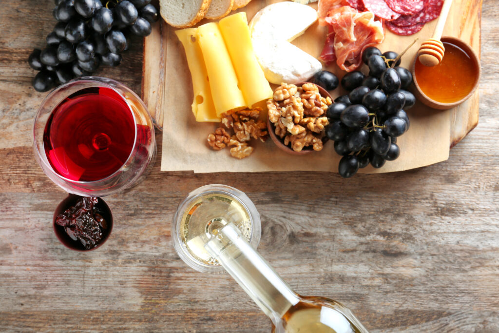 Pouring white wine into glass on table with delicious food, top view